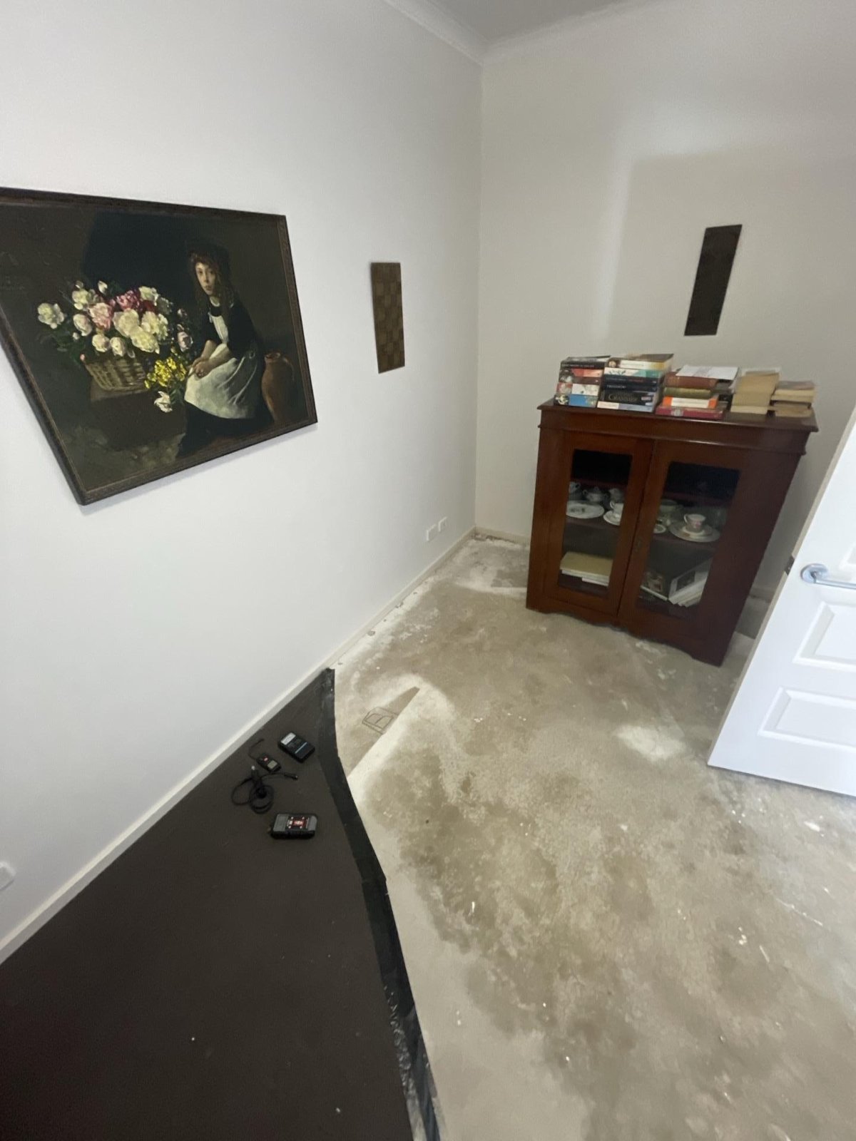 Stripped room floor with water staining and two moisture meters on the dark sheeting.
