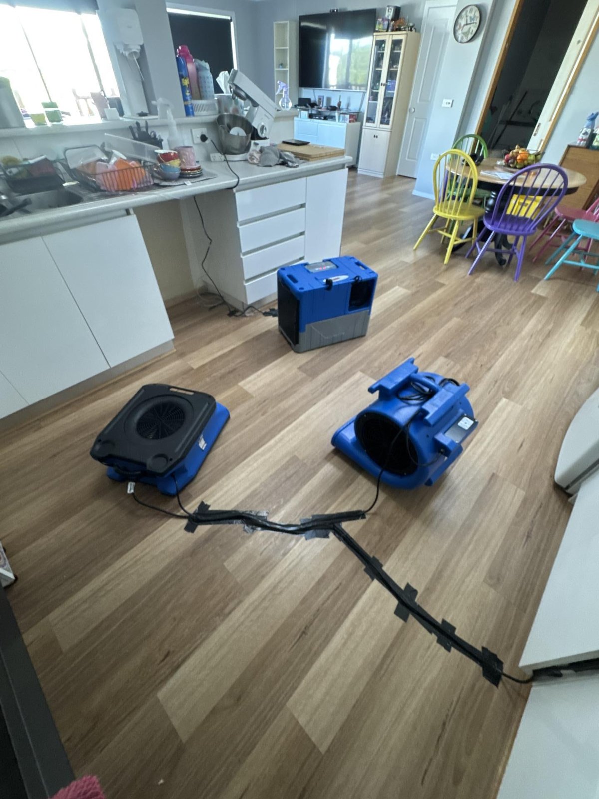 Two air movers and a dehumidifier drying a timber-look kitchen and dining floor