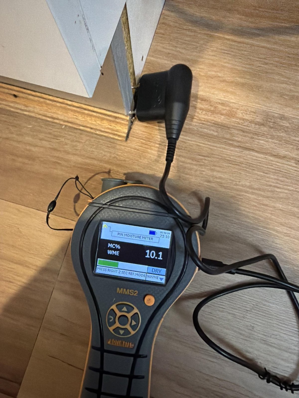 A technician checks skirting board moisture with a pin moisture meter on timber flooring.