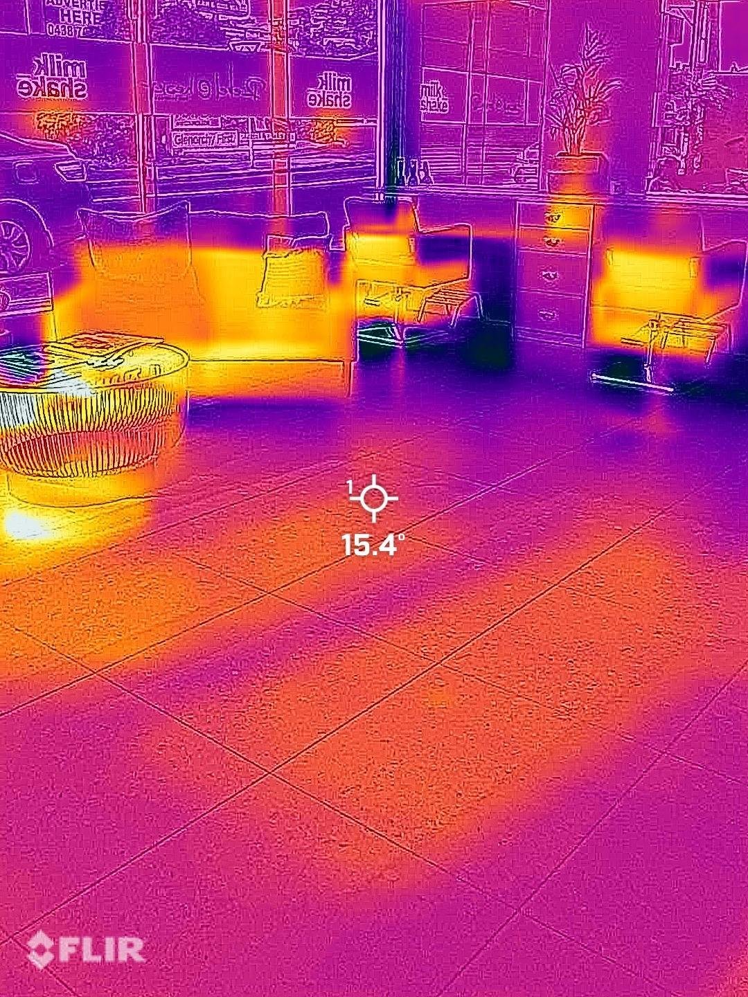 Thermal camera view of a tiled floor and furniture in a shopfront-style room, with a spot reading shown