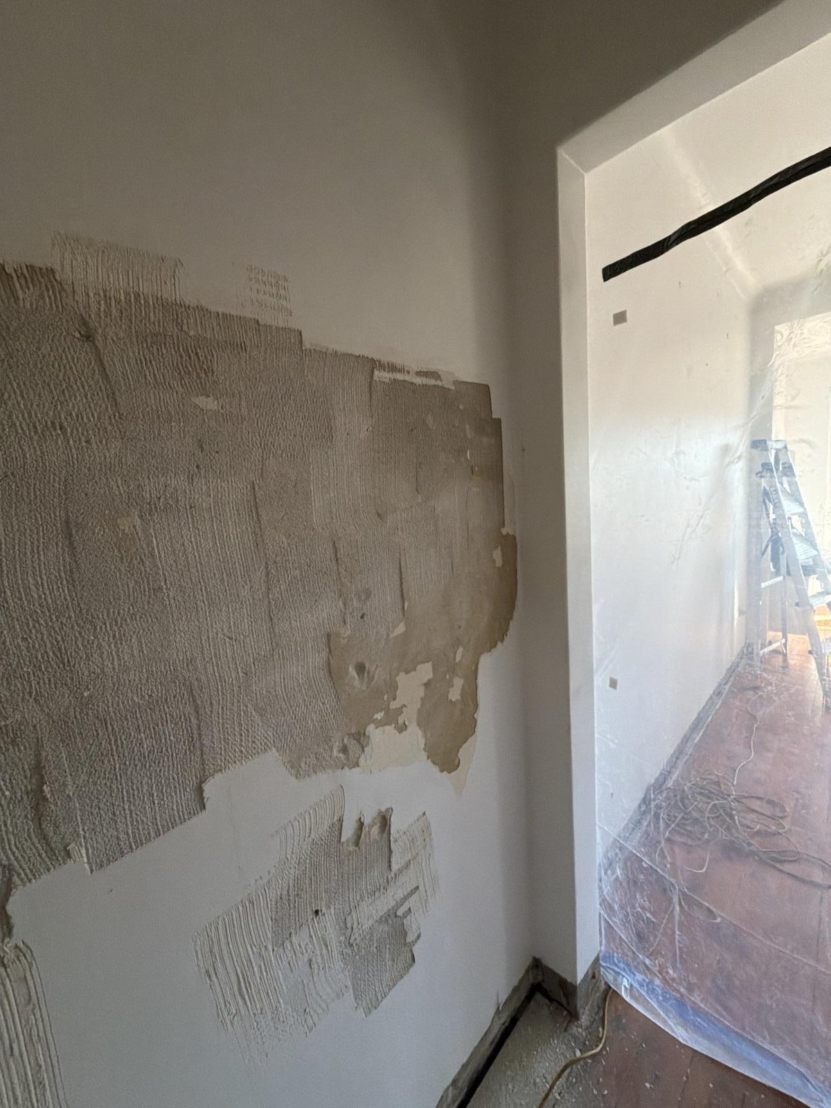 Stripped wall plaster and a plastic-covered doorway into a room with a ladder and cables