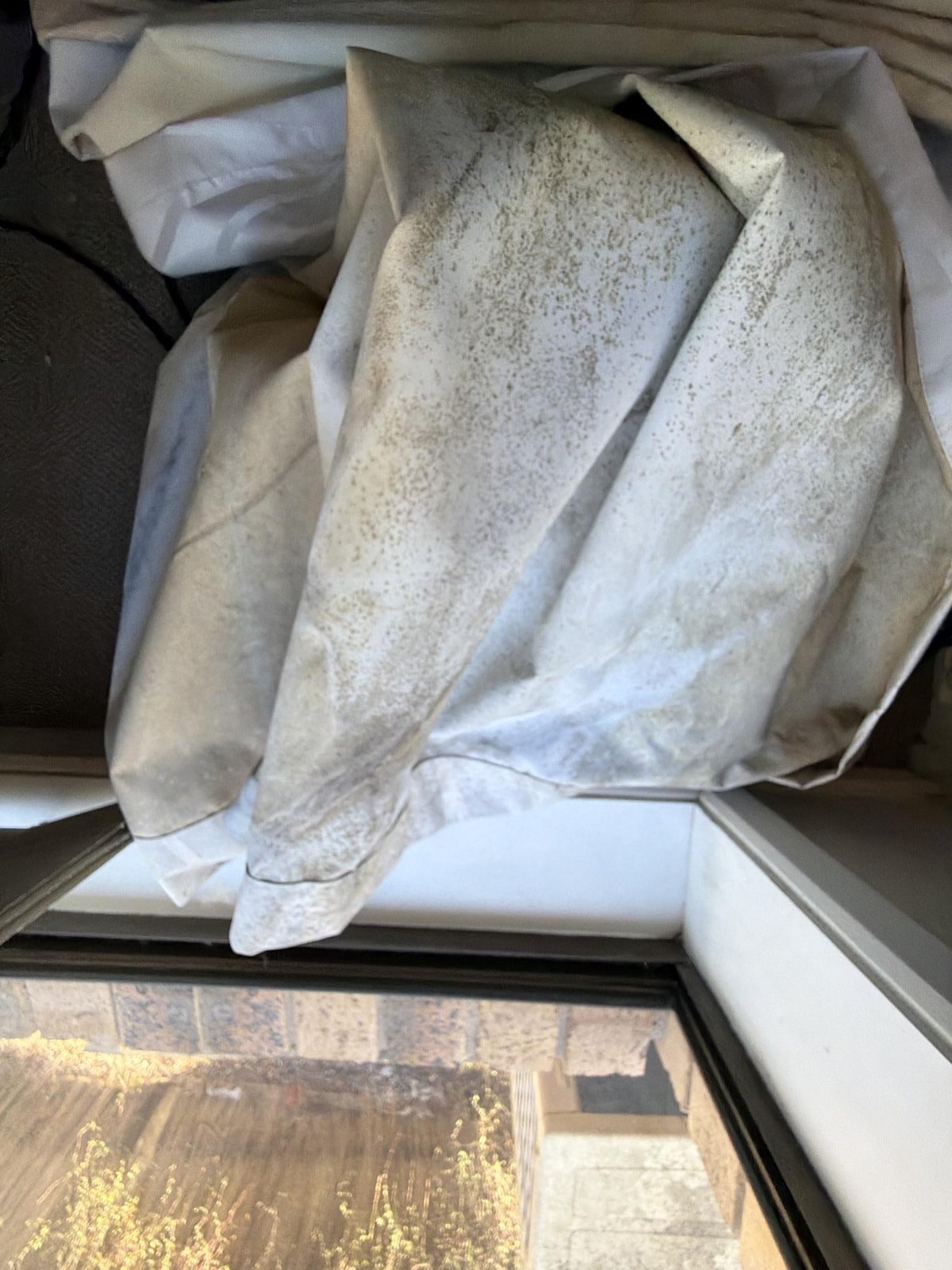 Mould-speckled bedding and fabric piled on a window sill beside a brick exterior.