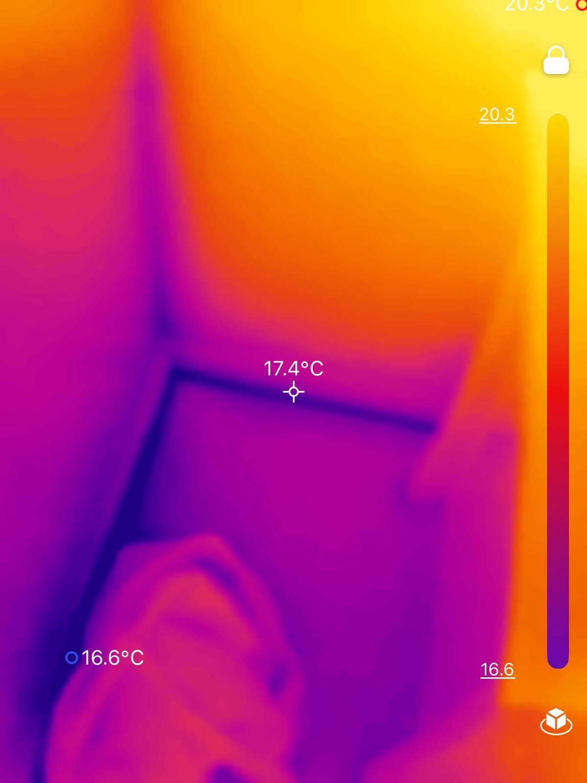 Thermal camera image of a wall corner and floor with temperature readings showing on screen