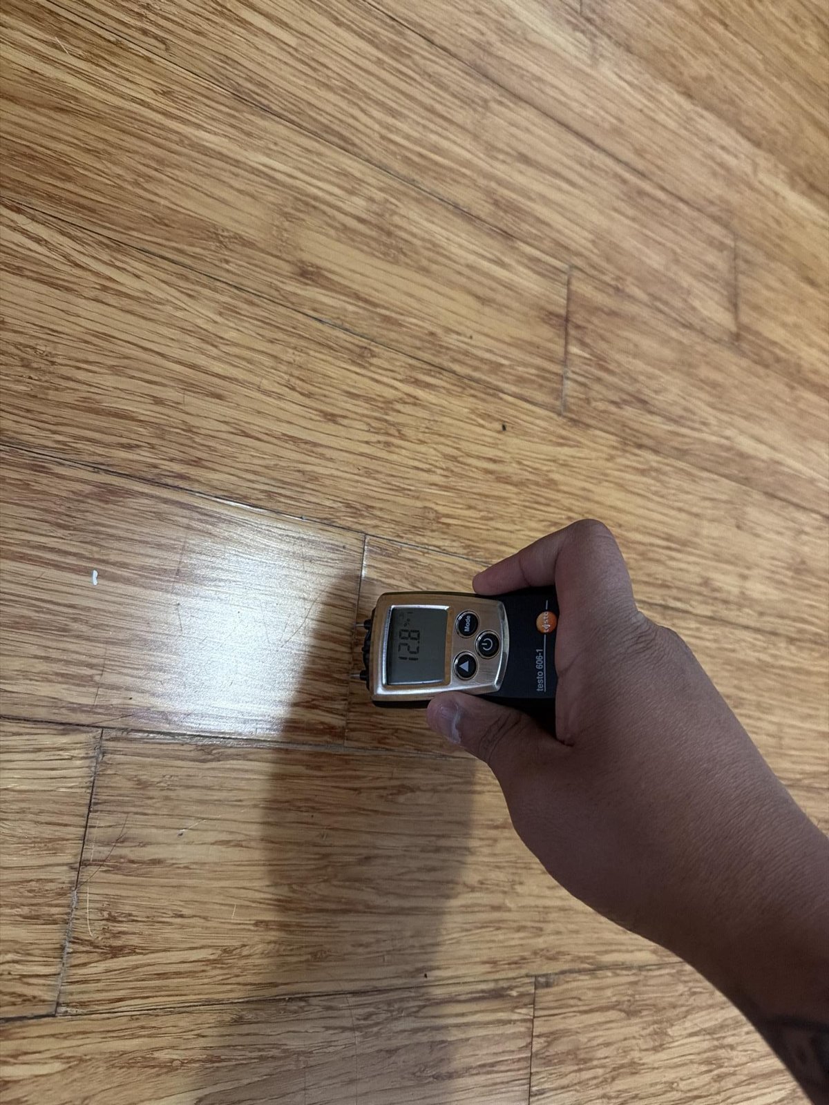 A hand holding a moisture meter against a timber-look floor to test the boards.