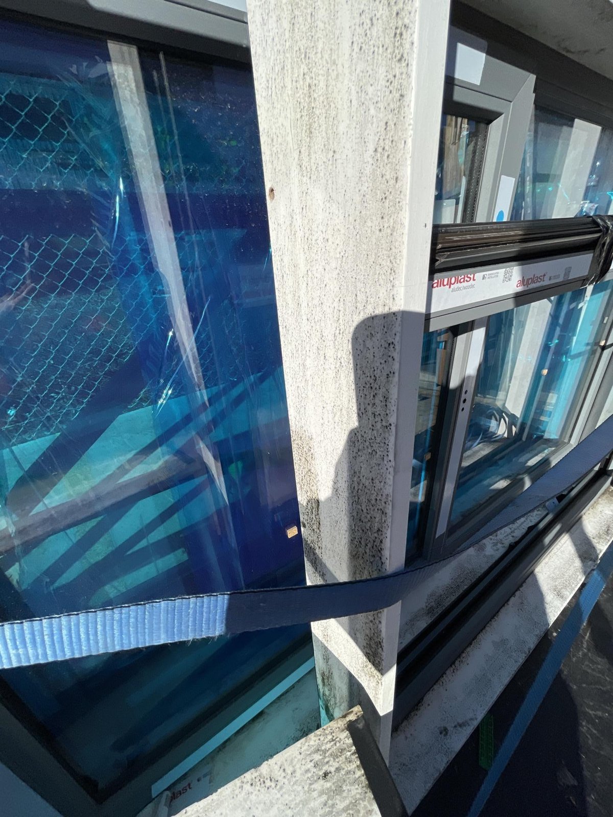 A stained concrete column beside aluminium-framed windows, with a blue strap across the glazing.