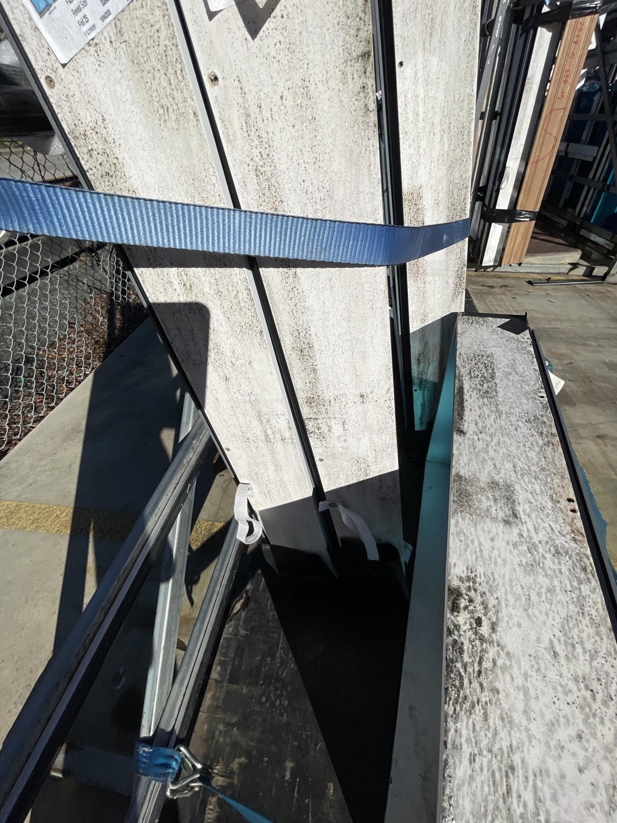 Stacked fibre cement sheets strapped to a rack on a yard, showing dark staining and mould growth.