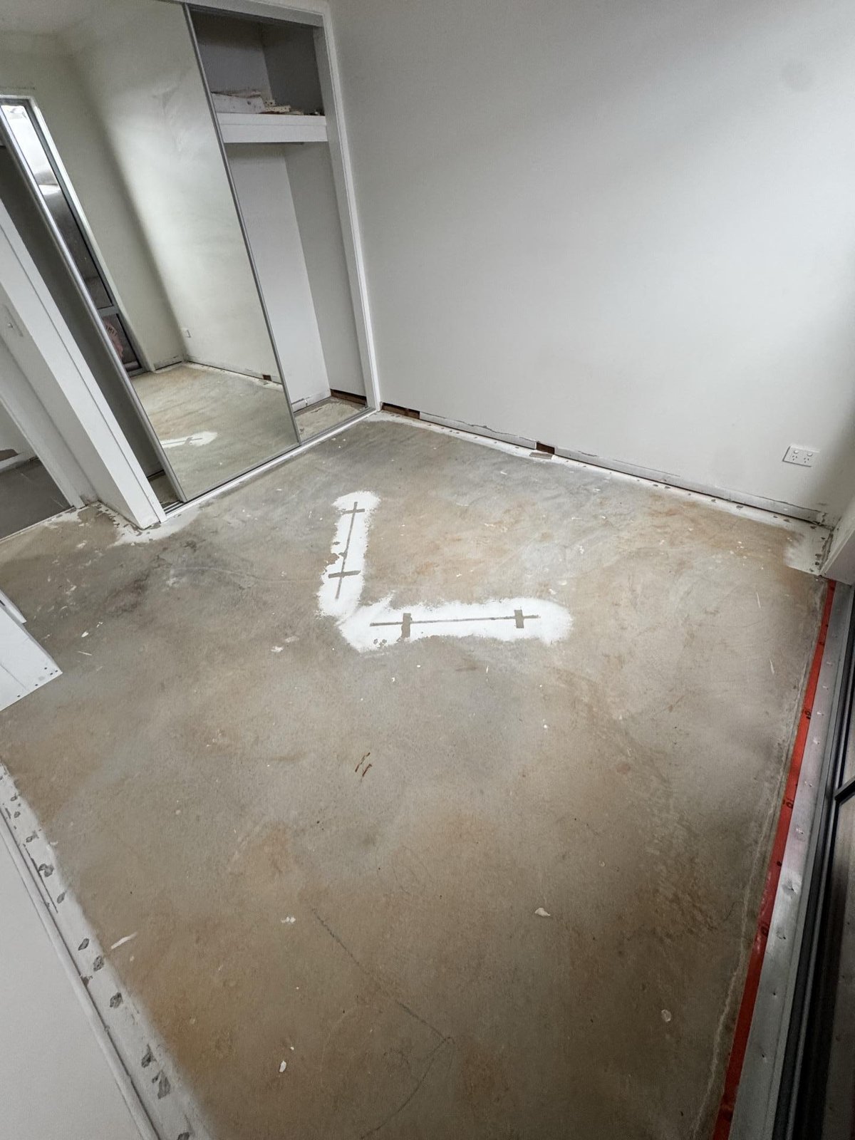 A stripped bedroom with bare concrete floor, cut-back wall linings and white marks on the slab.