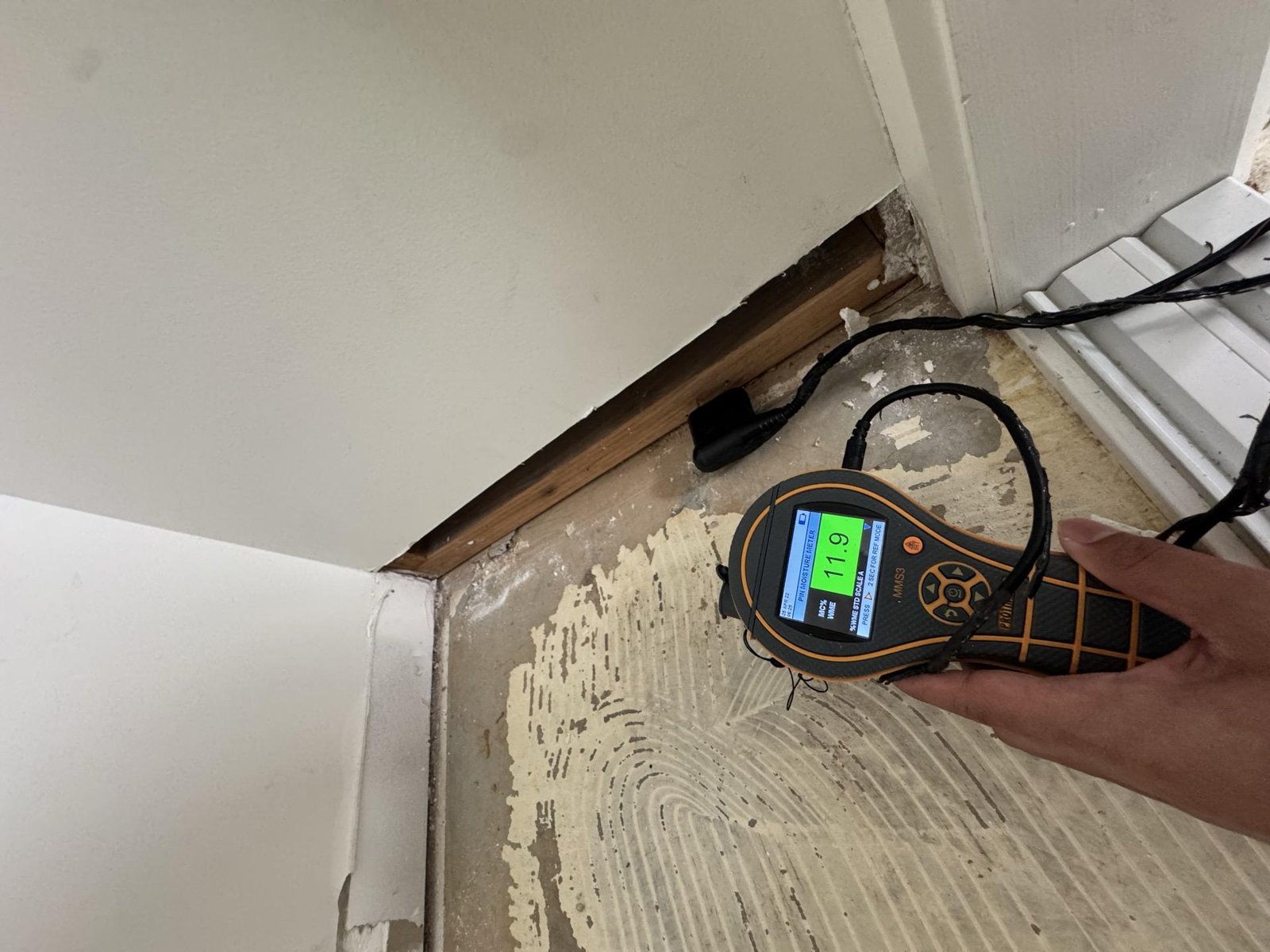 A technician checks moisture in a stripped floor and skirting board with a handheld meter.