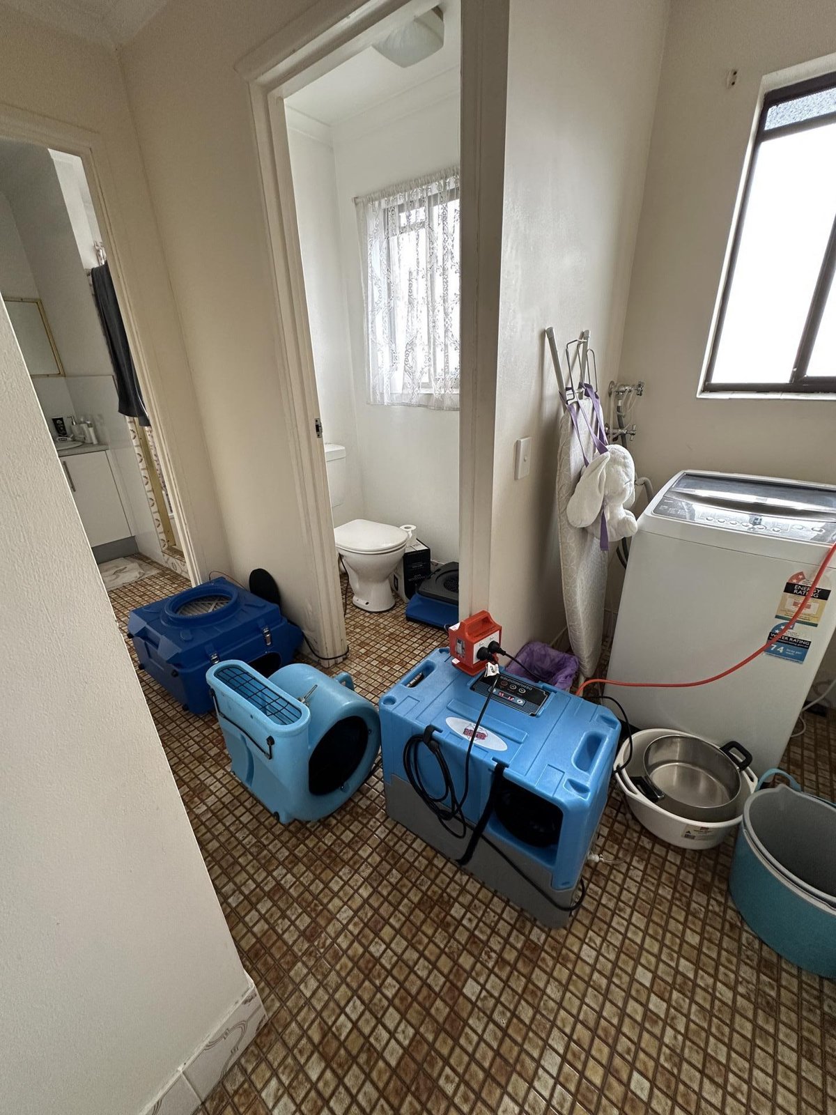 Blue air movers and a dehumidifier drying a laundry floor beside a washing machine