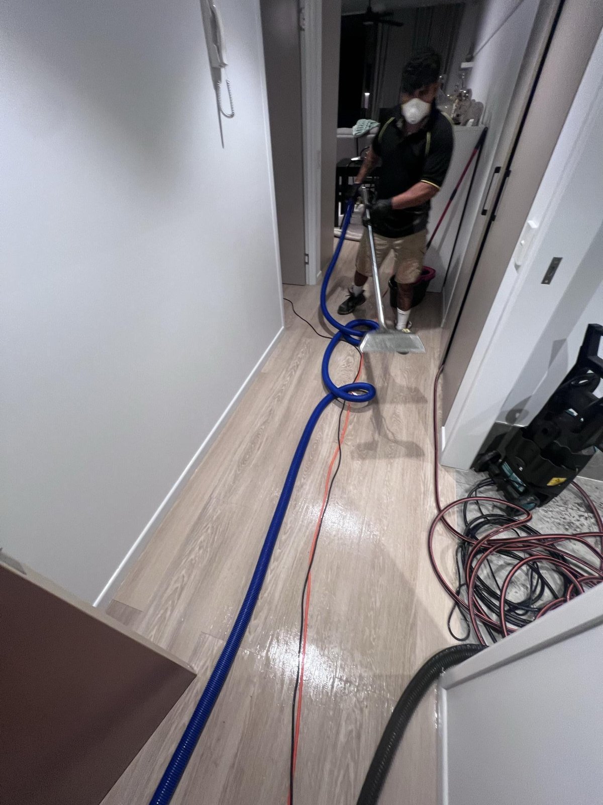 A technician extracting water from a hallway floor with a wand, a blue hose and an extractor running